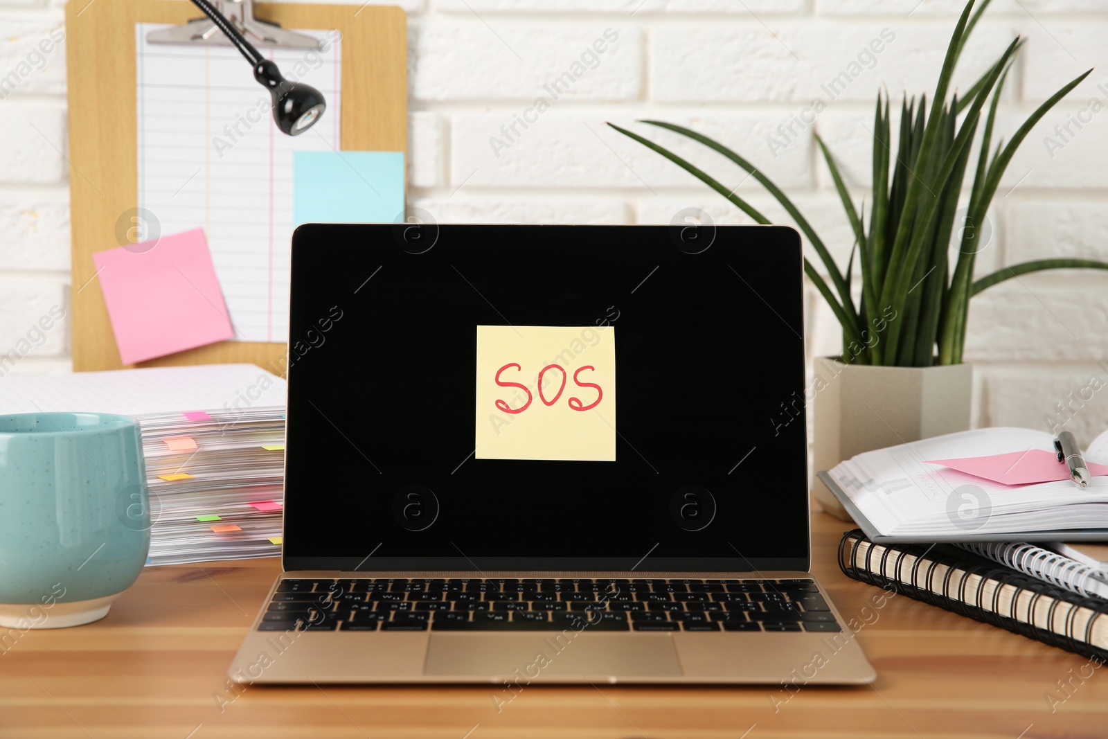 Photo of Note with word SOS, laptop and stationery on wooden table at workplace