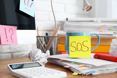 Photo of Note with word SOS, cup and stationery on wooden table at workplace