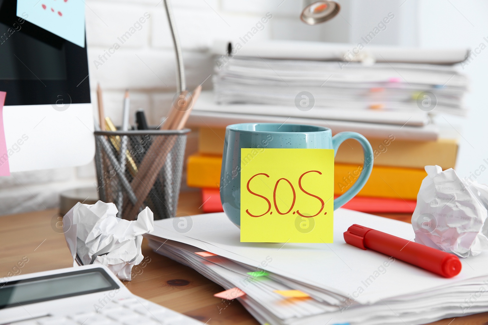 Photo of Note with word SOS, cup and stationery on wooden table at workplace