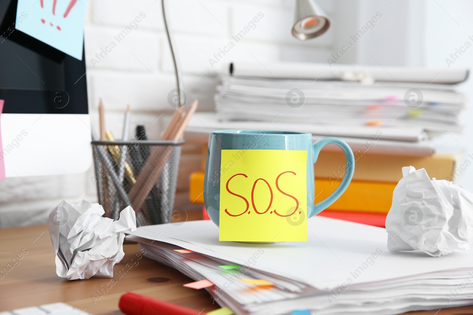 Photo of Note with word SOS, cup and stationery on wooden table at workplace