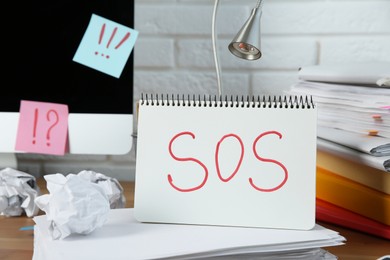 Photo of Notebook with word SOS and stationery on wooden table at workplace