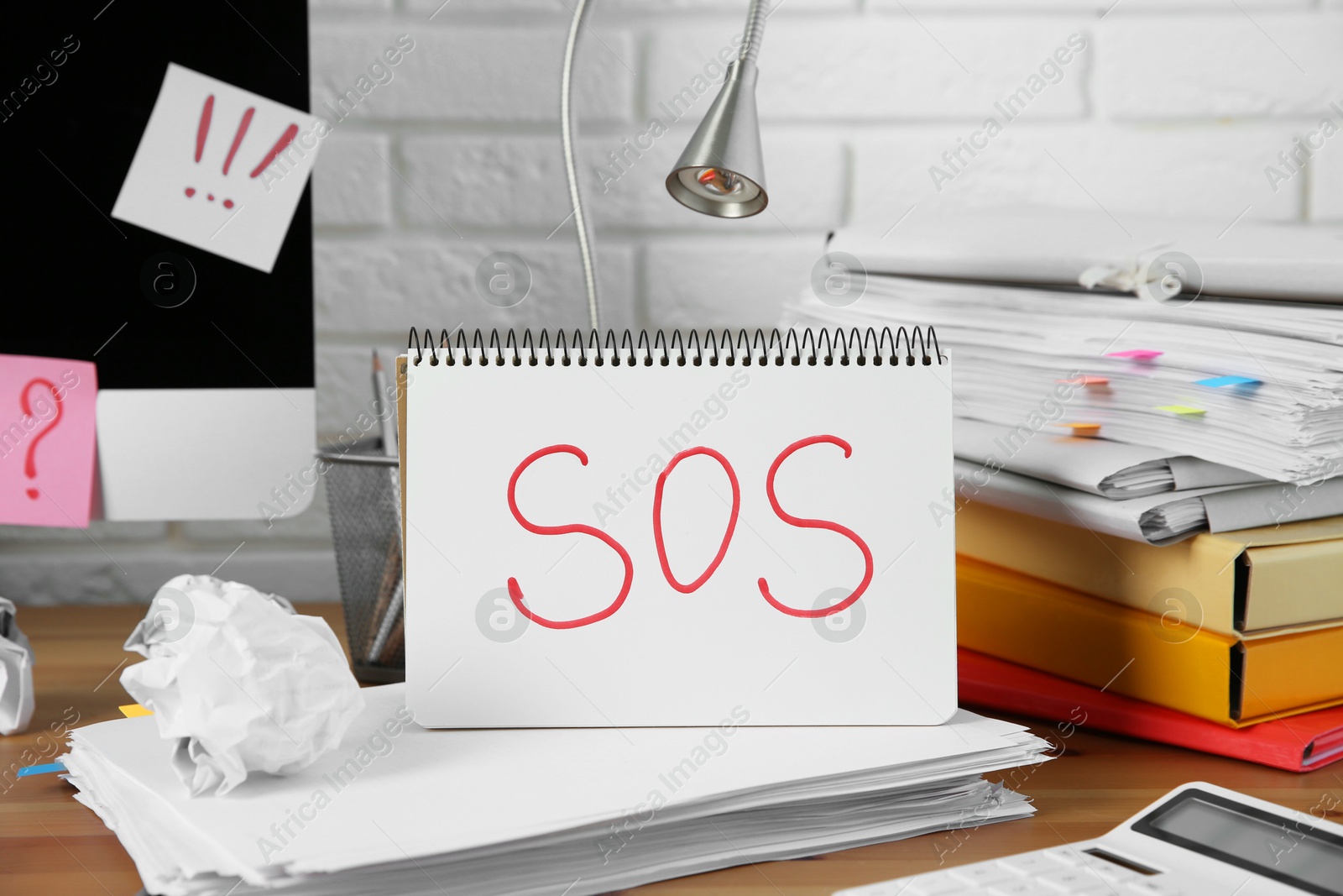 Photo of Notebook with word SOS and stationery on wooden table at workplace