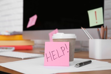 Photo of Note with word Help, cup and stationery on wooden table at workplace