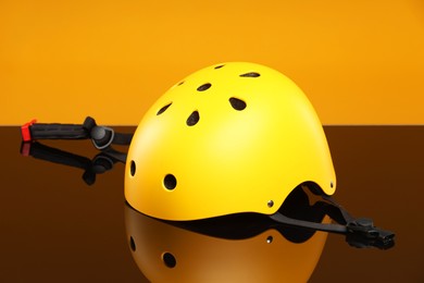 Photo of Stylish protective helmet on mirror surface against orange background