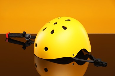 Stylish protective helmet on mirror surface against orange background