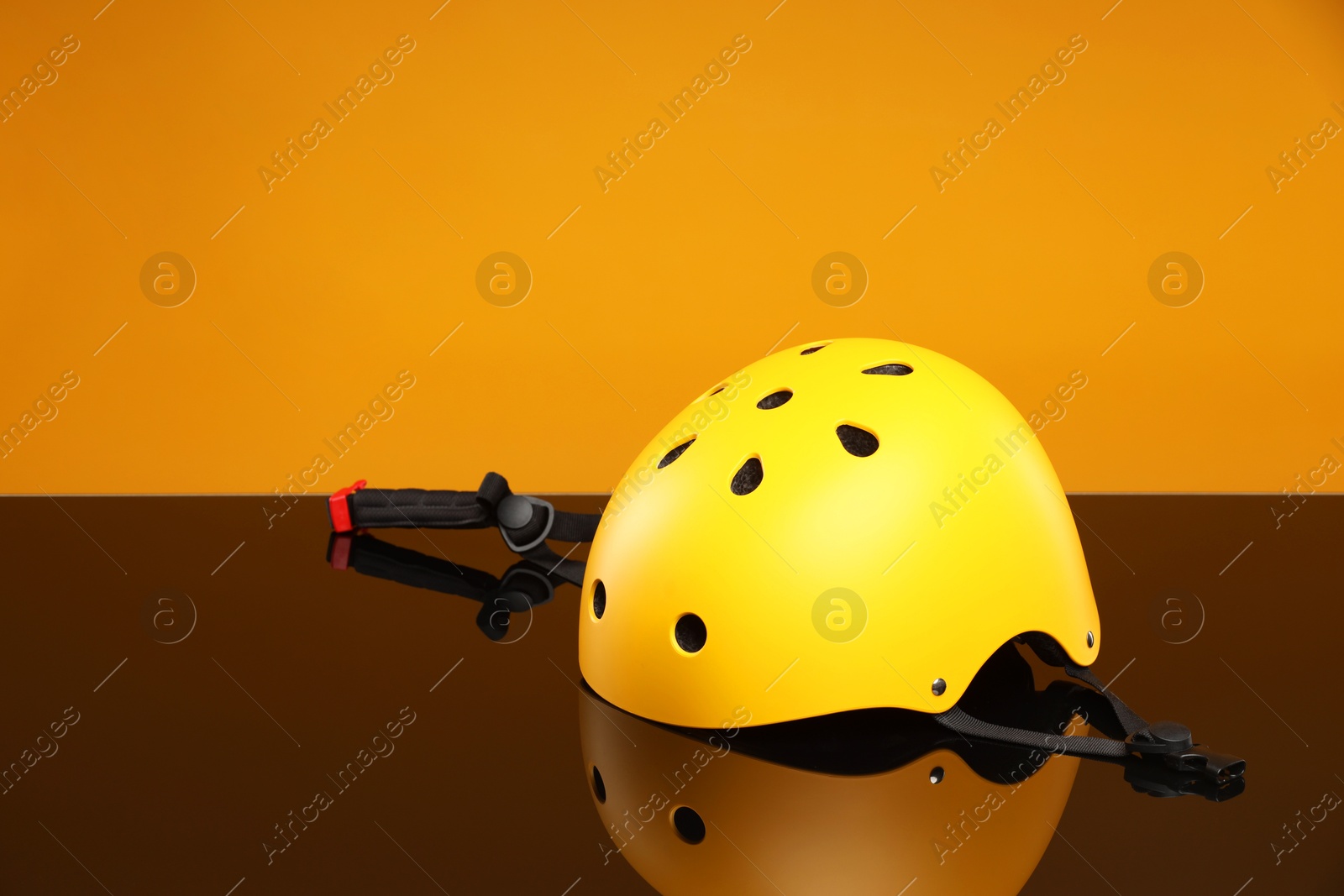 Photo of Stylish protective helmet on mirror surface against orange background. Space for text