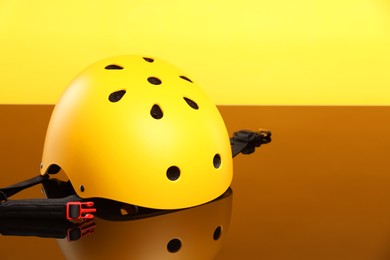 Stylish protective helmet on mirror surface against orange background. Space for text