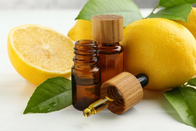 Photo of Essential oils in bottles, dropper, lemons and green leaves on white table, closeup