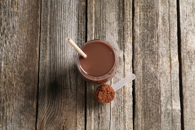 Delicious protein shake in glass and scoop with powder on wooden table, top view