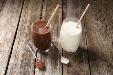 Delicious protein shakes in glasses and spoons with powder on wooden table