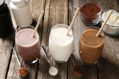 Photo of Delicious protein shakes in glasses, powder, spoons and plastic bottles on wooden table