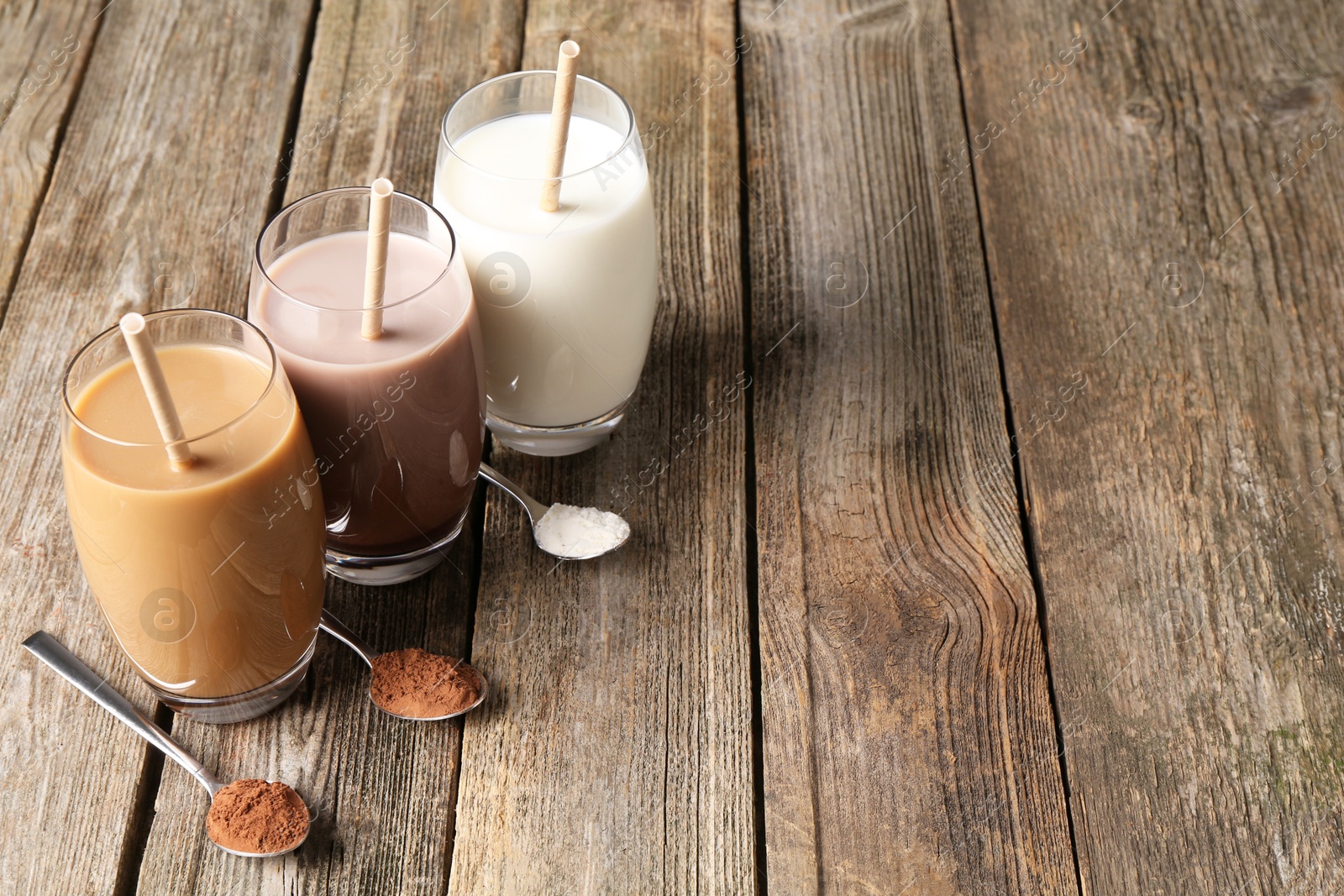 Photo of Delicious protein shakes in glasses and spoons with powder on wooden table, space for text