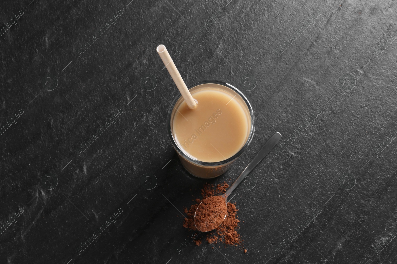 Photo of Delicious protein shake in glass and spoon with powder on black table, top view