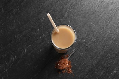 Photo of Delicious protein shake in glass and spoon with powder on black table, top view