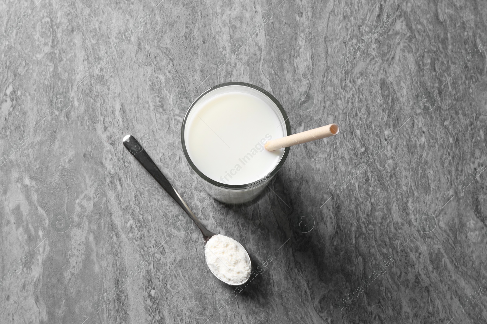 Photo of Delicious protein shake in glass and spoon with powder on grey table, top view