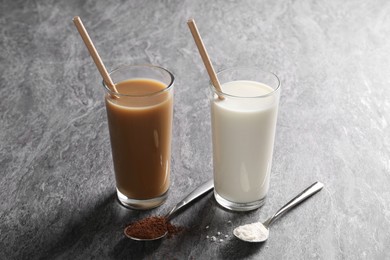 Delicious protein shakes in glasses and spoons with powder on grey table