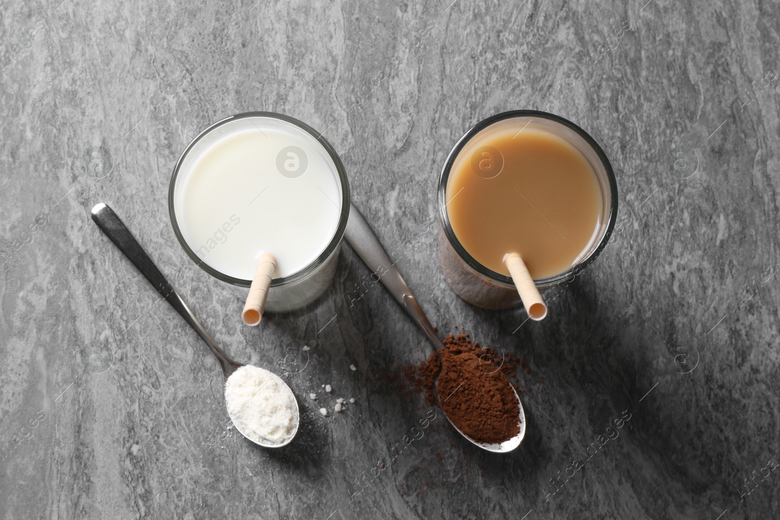 Photo of Delicious protein shakes in glasses and spoons with powder on grey table, flat lay