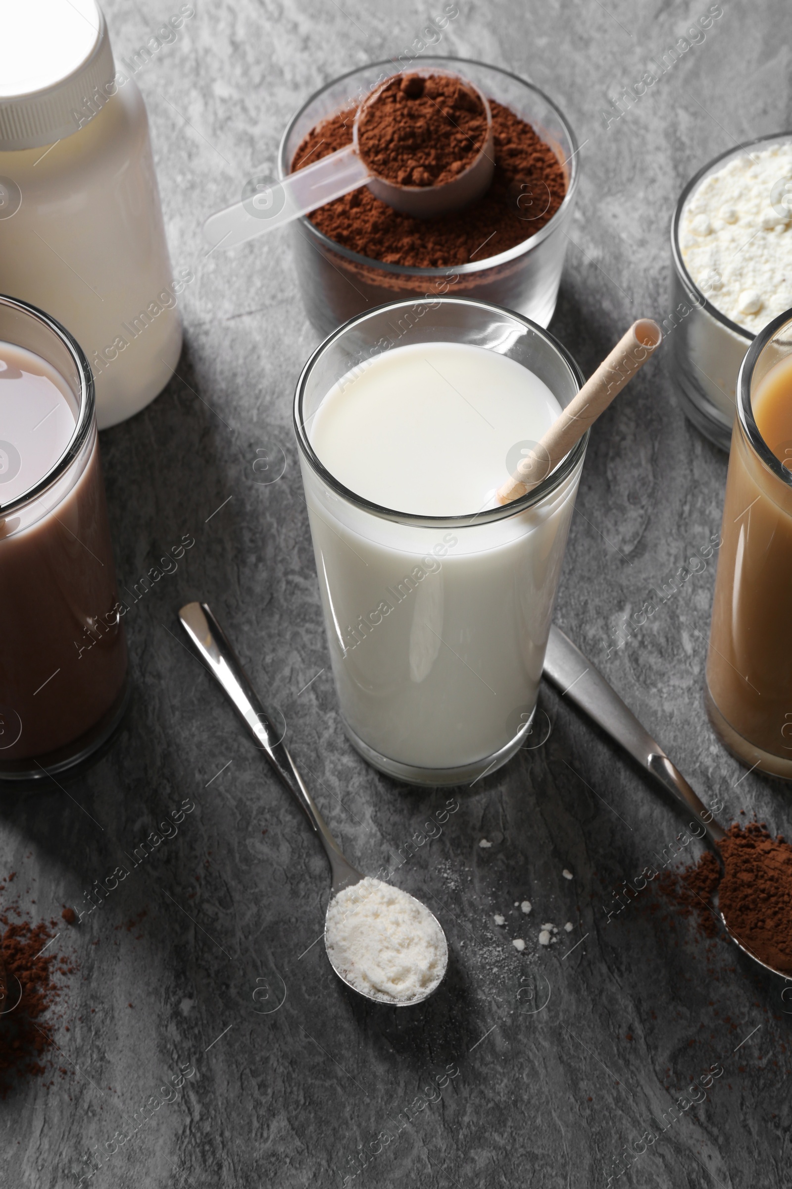 Photo of Delicious protein shakes in glasses, powder and spoons on grey table