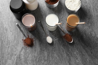 Photo of Delicious protein shakes in glasses, powder, spoons and plastic bottles on grey table, flat lay