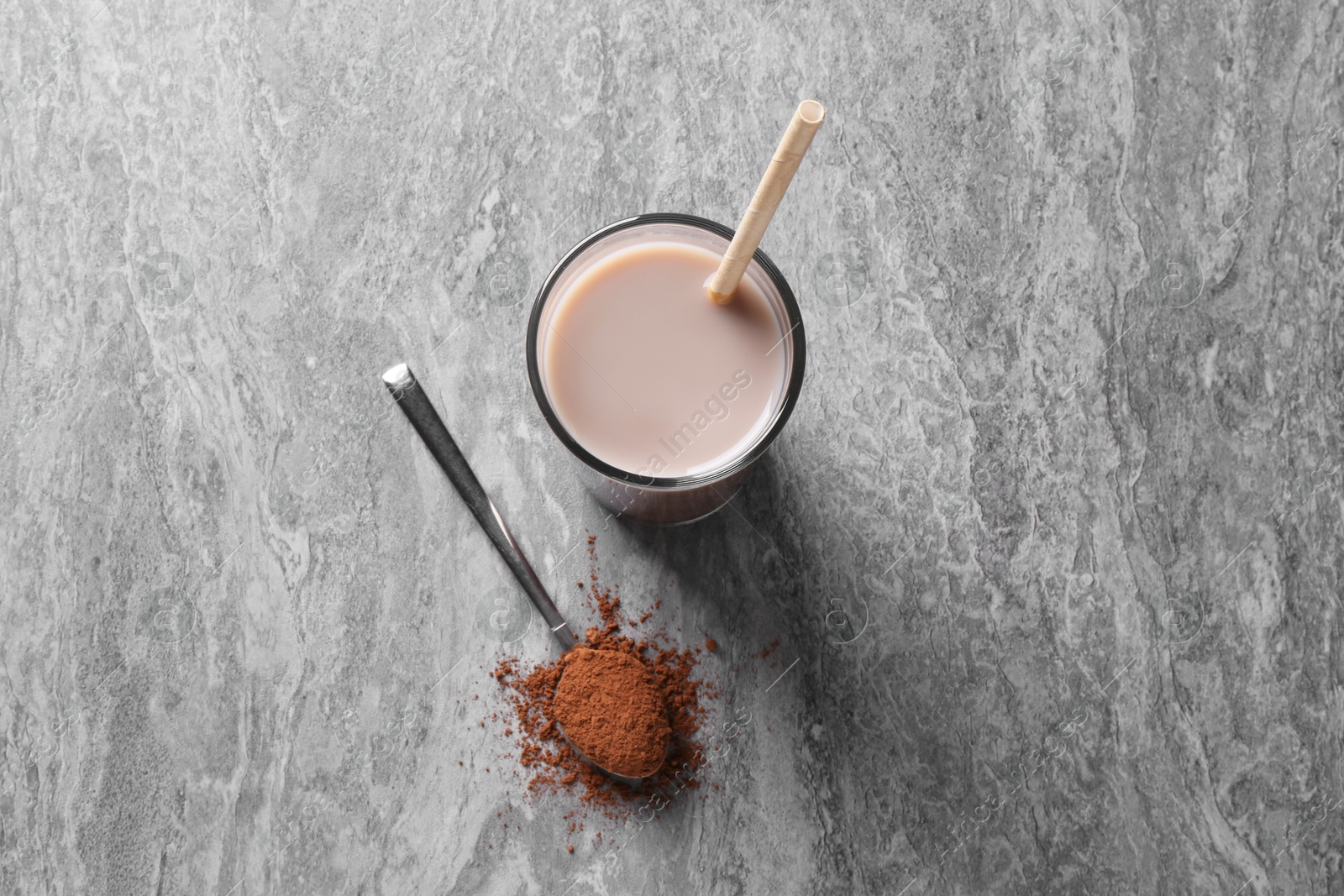 Photo of Delicious protein shake in glass and spoon with powder on grey table, top view