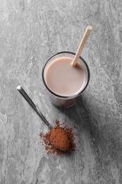 Photo of Delicious protein shake in glass and spoon with powder on grey table, top view