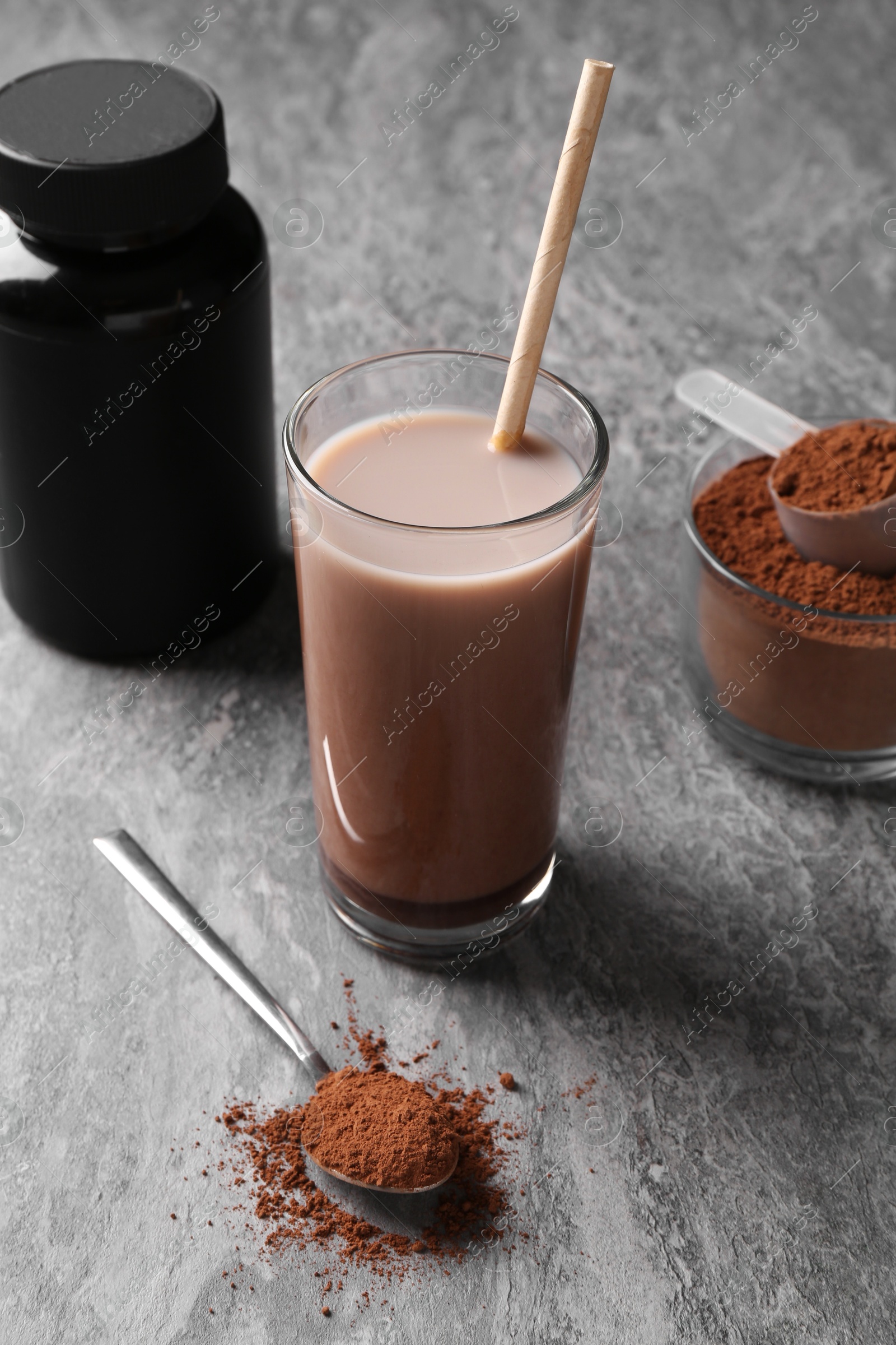 Photo of Delicious protein shake in glass, powder, spoon and plastic bottle on grey table