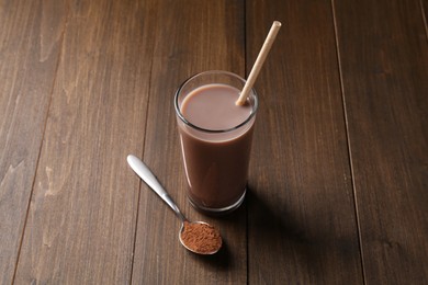 Photo of Delicious protein shake in glass and spoon with powder on wooden table