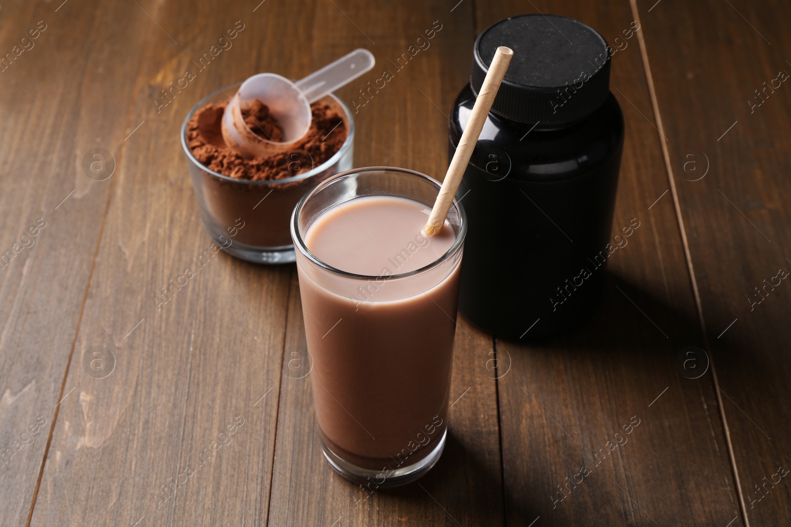 Photo of Delicious protein shake in glass, powder, scoop and plastic bottle on wooden table