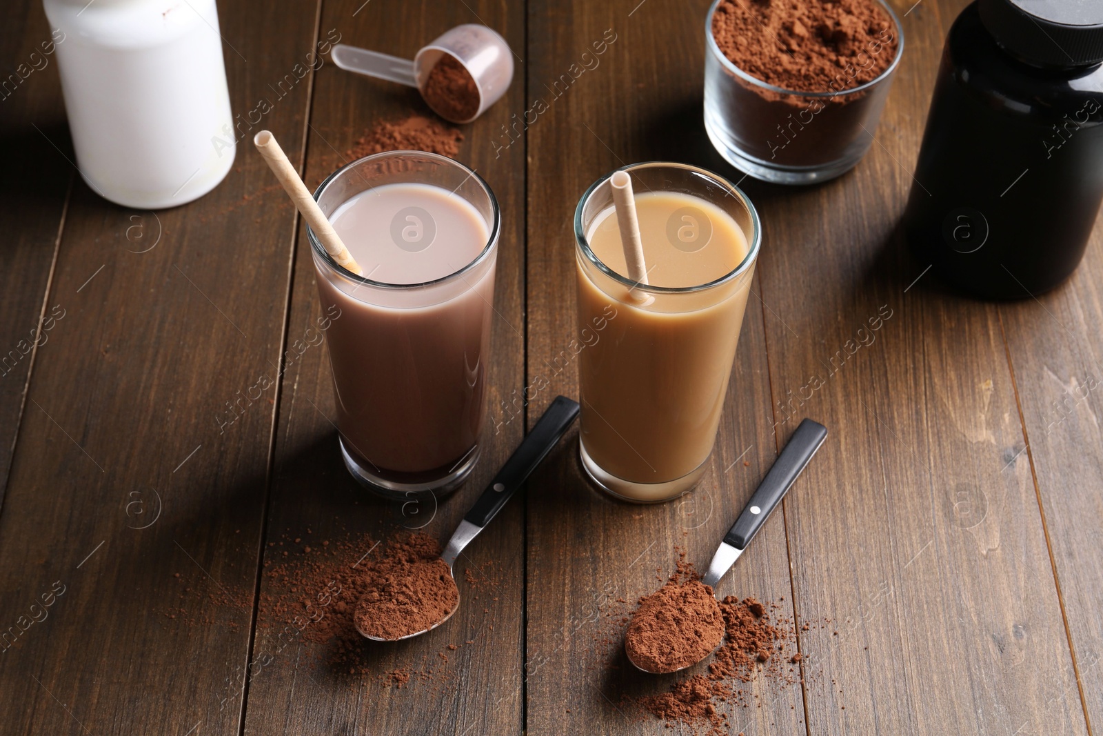 Photo of Delicious protein shakes in glasses, powder and spoons on wooden table