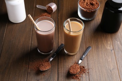 Photo of Delicious protein shakes in glasses, powder and spoons on wooden table