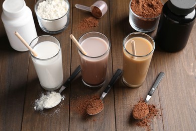 Photo of Delicious protein shakes in glasses, powder and spoons on wooden table