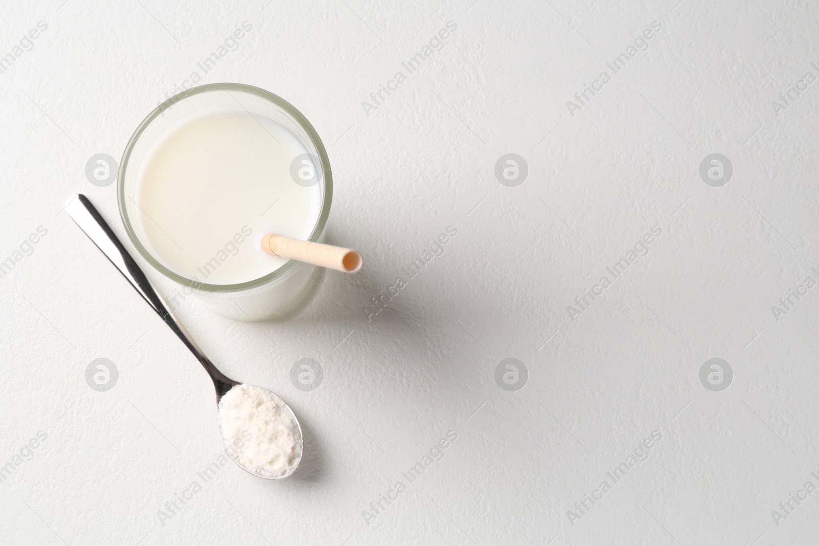 Photo of Delicious protein shake in glass and spoon with powder on white background, top view. Space for text