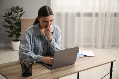 Embarrassed woman working with laptop at wooden table in office