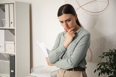 Photo of Embarrassed young woman with document in office