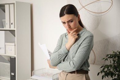 Embarrassed young woman with document in office