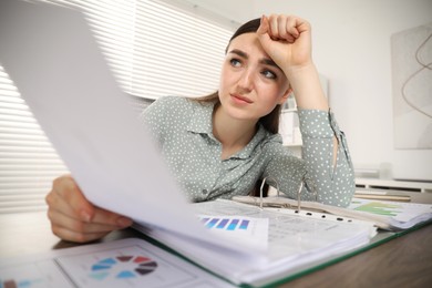 Photo of Embarrassed woman with document at table in office