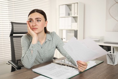 Embarrassed woman with documents at wooden table in office