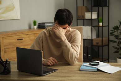 Embarrassed man at wooden table with laptop in office