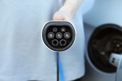 Photo of Man with power supply cable at electric car charging station outdoors, closeup