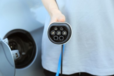 Photo of Man with power supply cable at electric car charging station outdoors, closeup