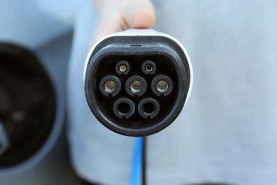 Photo of Man with power supply cable at electric car charging station outdoors, closeup