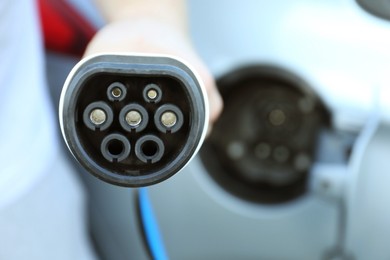 Photo of Man with power supply cable at electric car charging station outdoors, closeup