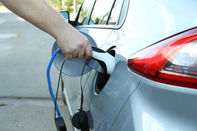 Photo of Man inserting plug into electric car socket at charging station outdoors, closeup