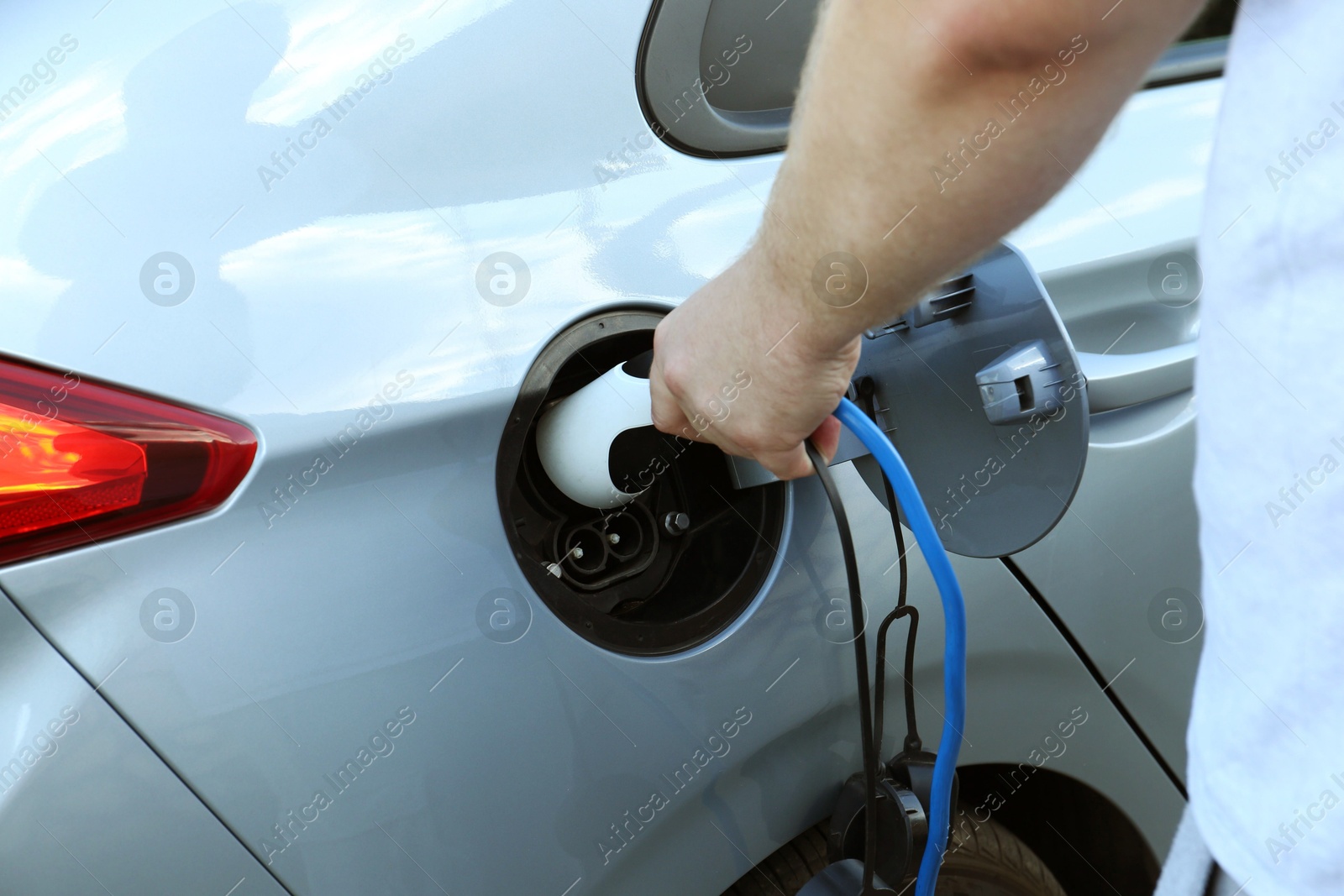 Photo of Man inserting plug into electric car socket at charging station outdoors, closeup