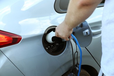 Man inserting plug into electric car socket at charging station outdoors, closeup