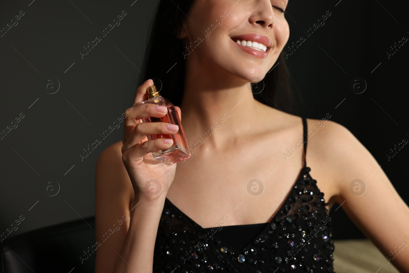 Photo of Smiling woman with bottle of perfume on dark background, closeup