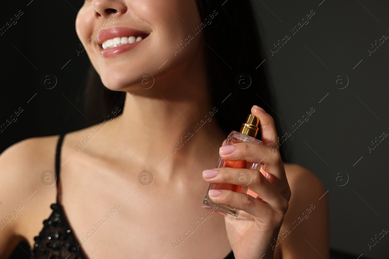 Photo of Smiling woman with bottle of perfume on dark background, closeup