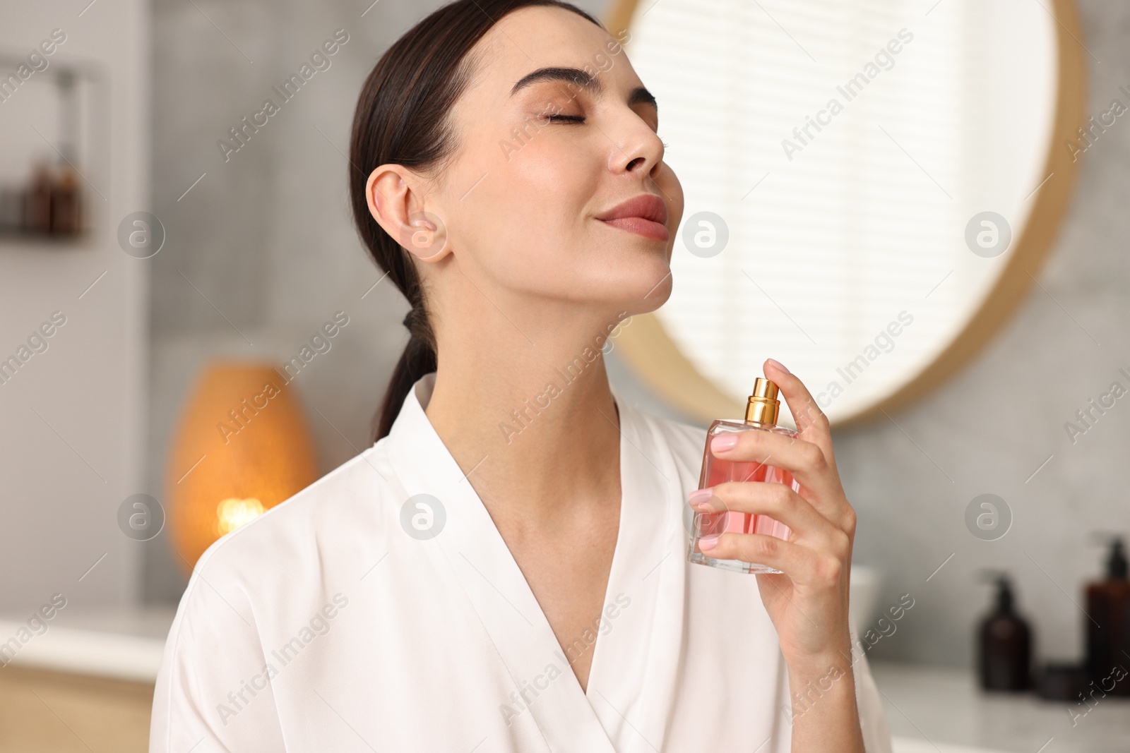 Photo of Beautiful woman spraying aromatic perfume in bathroom