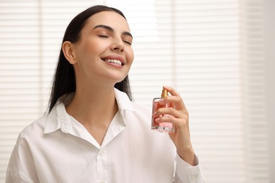 Smiling woman spraying aromatic perfume at home. Space for text