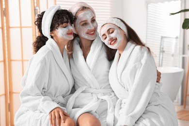 Photo of Happy friends in bathrobes with facial masks indoors. Spa party